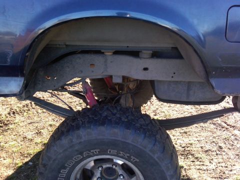 1988 Ford Bronco - Close-up of the rear suspension and tire of a blue truck, showing leaf springs and a shock absorber.