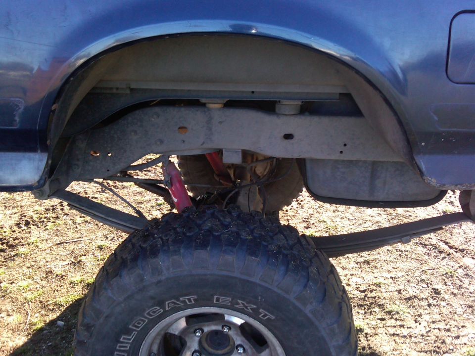 Rear leaf springs, red shock absorber, and large tire on a blue truck