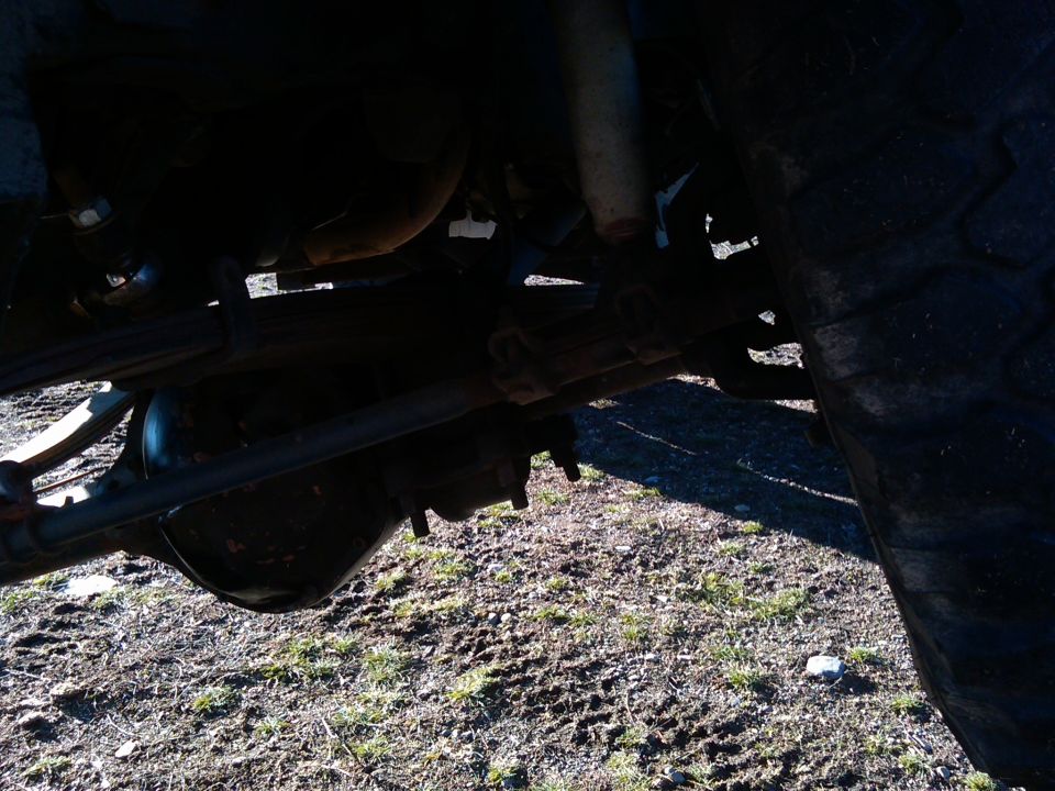 Close-up of a vehicle's rear axle, leaf springs, and shock absorber. A large tire is visible on the right
