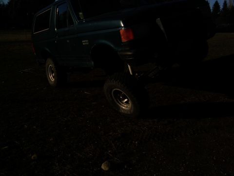 1988 Ford Bronco - A lifted green Ford Bronco sits on uneven terrain in low light conditions.