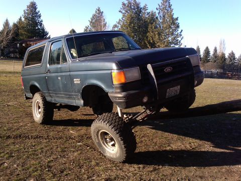 1988 Ford Bronco - A modified Ford Bronco with its front right tire on a log, demonstrating its suspension capabilities.