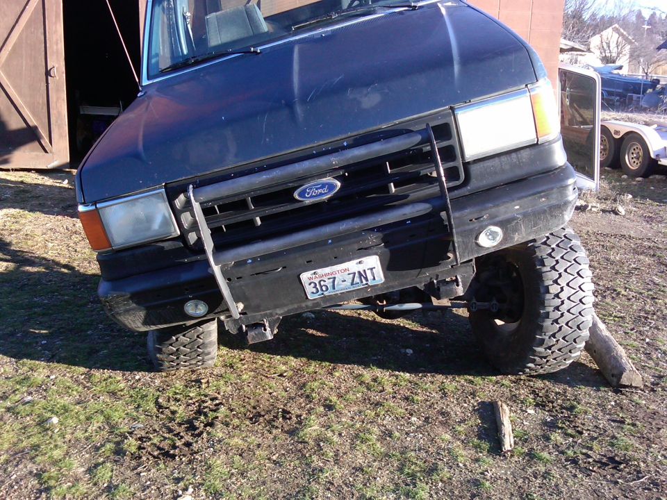 Dark blue 1988 Ford Bronco, 3q-front view, with front passenger wheel on a log