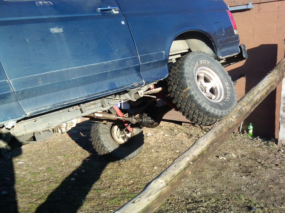 Side view of blue 1988 Ford Bronco with large tires on a wooden obstacle