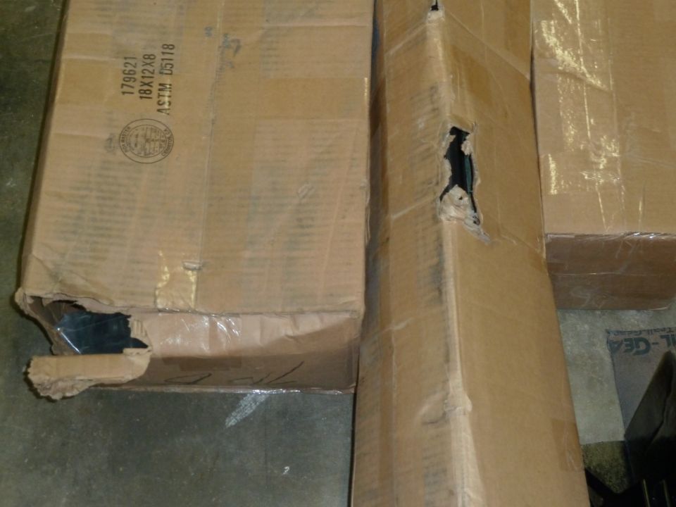 Torn and punctured cardboard shipping boxes on a concrete floor showing freight damage