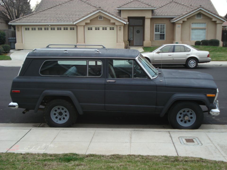 Dark colored Jeep Wagoneer parked on street, silver sedan in background