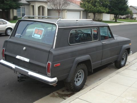 1977 Jeep Cherokee - A dark gray Jeep Wagoneer is parked on the side of a street with a 'For Sale' sign visible in the back window.