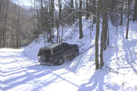 1995 Ford Bronco - A Ford Bronco navigates a snow-covered path through a wooded area.