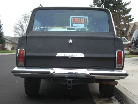 1977 Jeep Cherokee - Rear view of a black 1977 Jeep Cherokee, displaying a 'FOR SALE' sign in the window.