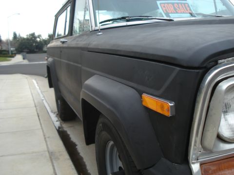 1977 Jeep Cherokee - A black 1977 Jeep Cherokee is parked curbside, displaying a 'FOR SALE' sign in the windshield.