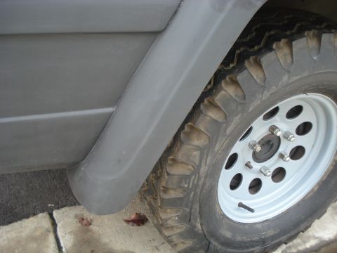 1977 Jeep Cherokee - A close-up view of the side of a vehicle, focusing on the fender and a tire on a white rim.