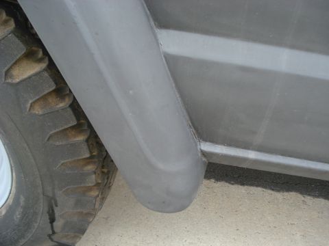 1977 Jeep Cherokee - Close-up view of a vehicle's side panel and wheel well, with visible tire tread and gray paint.