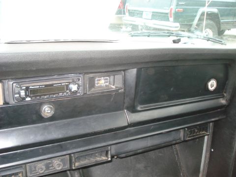 1977 Jeep Cherokee - The interior dashboard of a 1977 Jeep Cherokee features an aftermarket Pioneer stereo and a clock, with another Jeep visible through the wi…