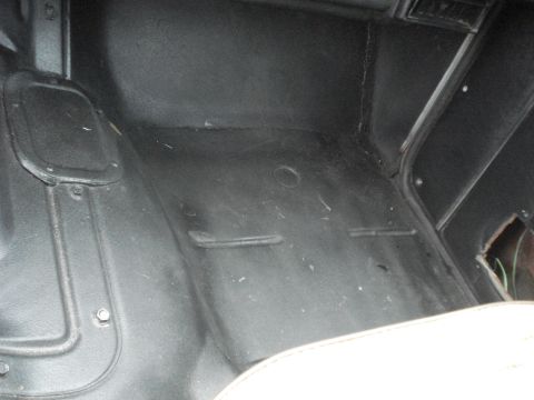1977 Jeep Cherokee - The interior floor of a vehicle shows a worn black mat with some debris and a partial view of a white seat.