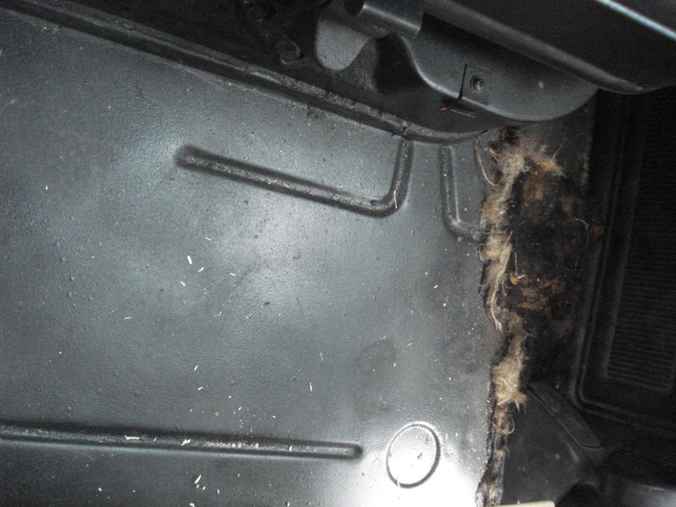 Close-up of a vehicle's floor, showing metal panels and some debris and insulation on the right side