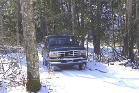1995 Ford Bronco - A 1995 Ford Bronco navigates a snow-covered road surrounded by dense woods.