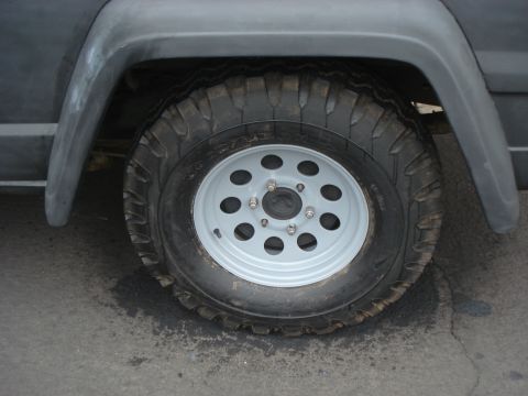 1977 Jeep Cherokee - Close-up of a 1977 Jeep Cherokee's front wheel and fender, showing a gray primer finish.