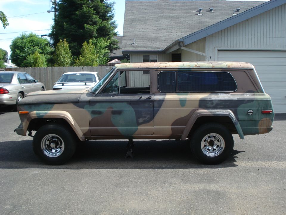 Camouflaged Jeep Cherokee with aftermarket wheels, jacked up on the driver's side