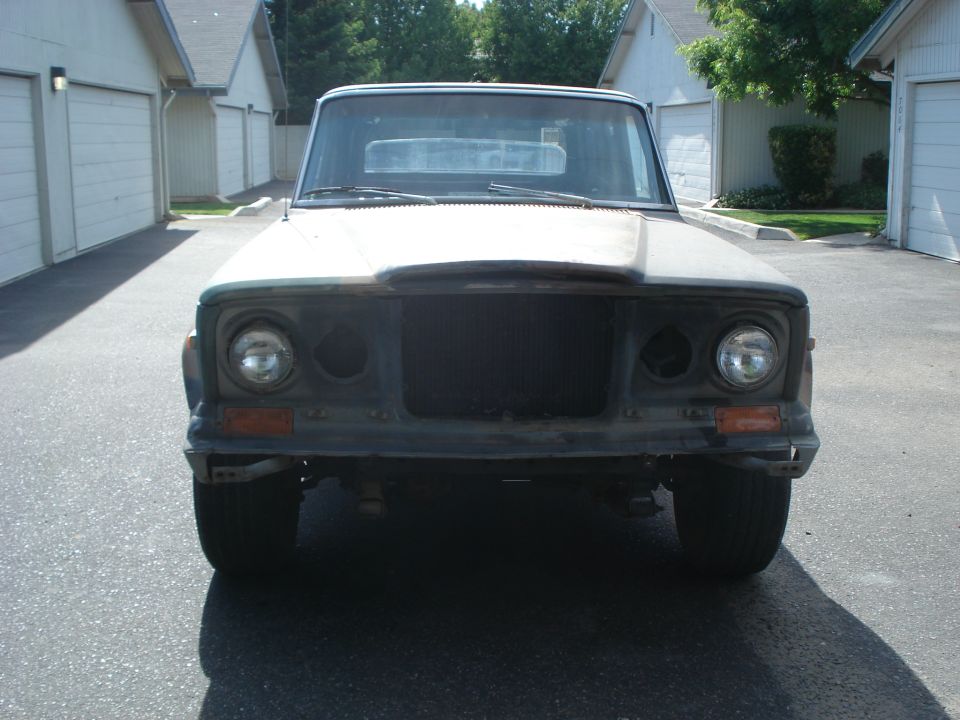 Front view of a Jeep J-series pickup truck, likely from the 1970s, with missing headlights and grille