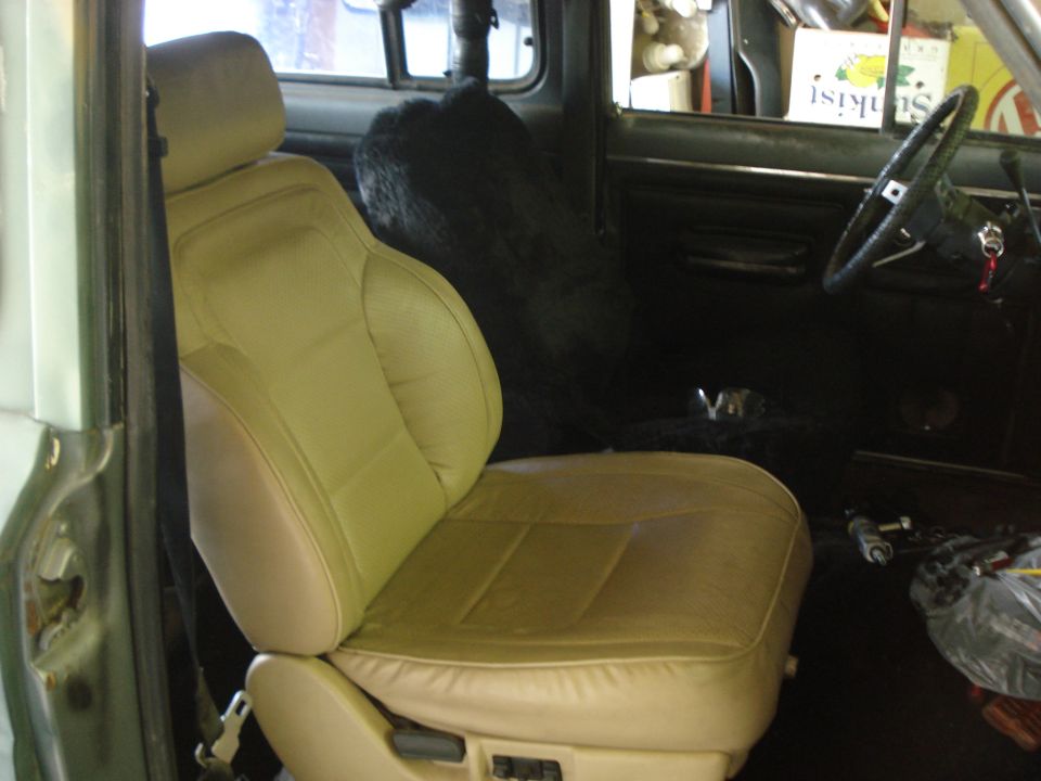 Tan leather bucket seat installed in a vehicle interior, viewed through the open passenger door during work.