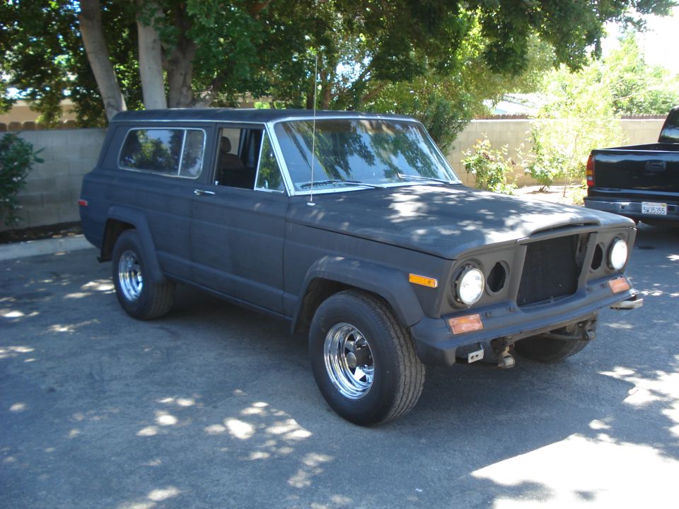 Dark matte Jeep Wagoneer, front passenger side view, chrome wheels, missing grille insert