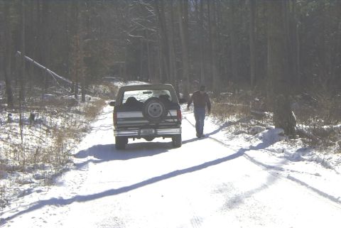 1995 Ford Bronco - A 1995 Ford Bronco drives down a snow-covered road in a wooded area.