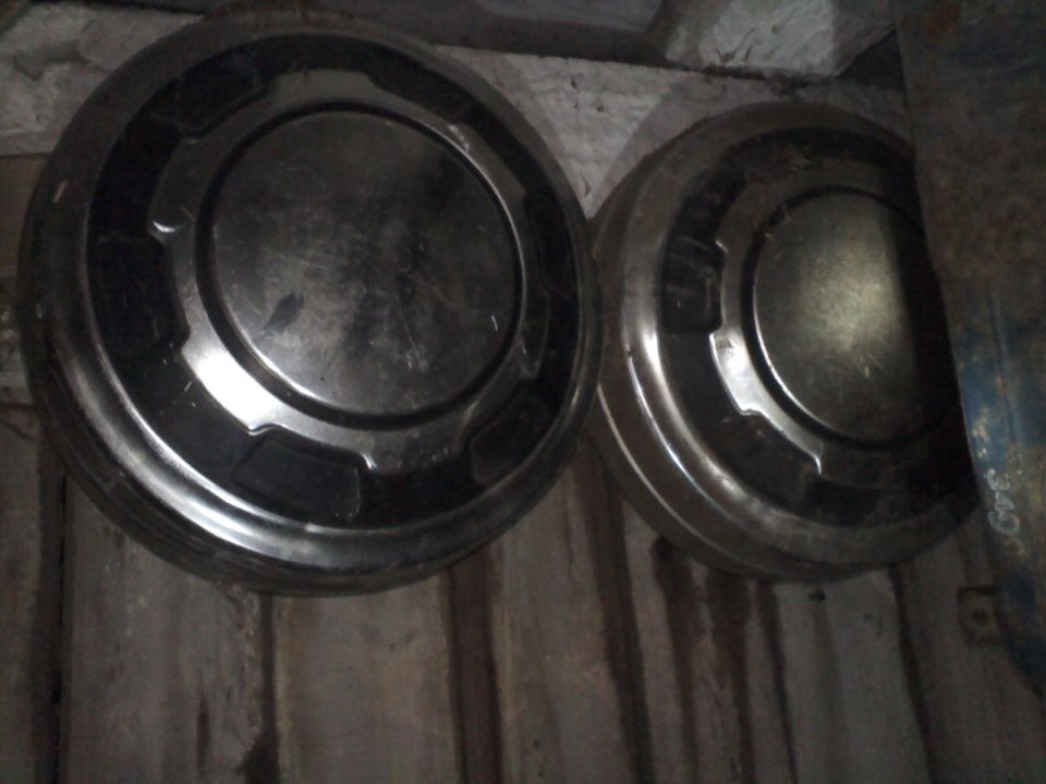 Two dusty chrome dog-dish hubcaps lying on weathered wood planks