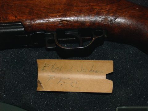 2003 Ford Crown Victoria - A close-up view of a rifle's wooden stock and trigger assembly, with a handwritten note identifying 'Ebal J. Johnson P.F.C.'