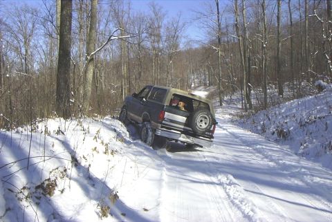 1995 Ford Bronco - A dog watches from the back of a Ford Bronco as it navigates a snow-covered forest road.