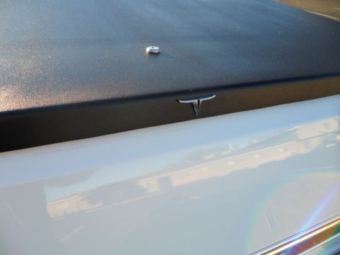1973 Ford Ranchero - Close-up of a black tonneau cover with a T-shaped emblem on the side of a white pickup truck.