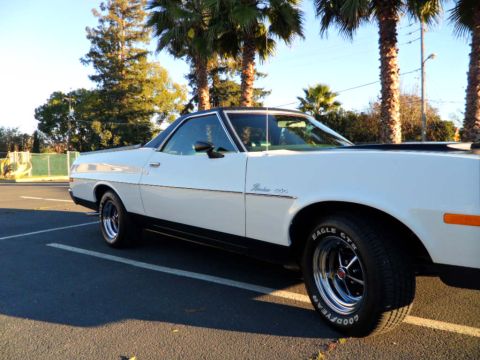1973 Ford Ranchero - A white 1973 Ford Ranchero is parked in a lot, with palm trees visible behind it.