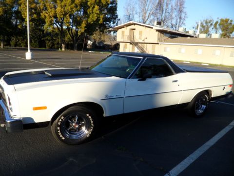 1973 Ford Ranchero - A white 1973 Ford Ranchero with a black hood stripe and vinyl top is parked in a lot.