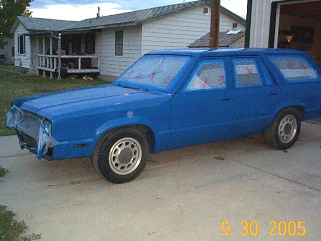 Blue station wagon, possibly a 1982 Mercury Zephyr, parked in a driveway. Windows are taped off for painting