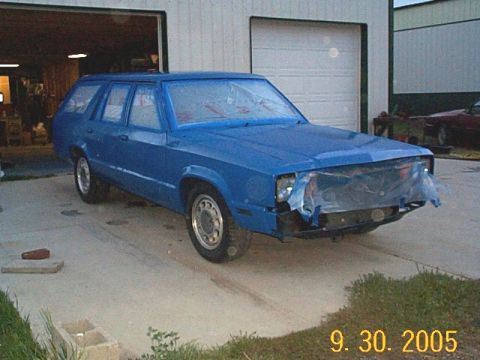 1982 Mercury Zephyr - A blue station wagon is parked outside a garage, its front end covered in protective plastic sheeting.