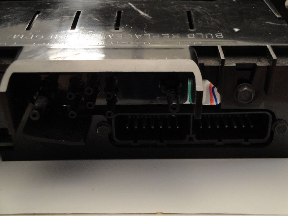 Back of an automotive instrument cluster showing electrical connectors and wiring. Text reads 'BULB REPLACE ME'
