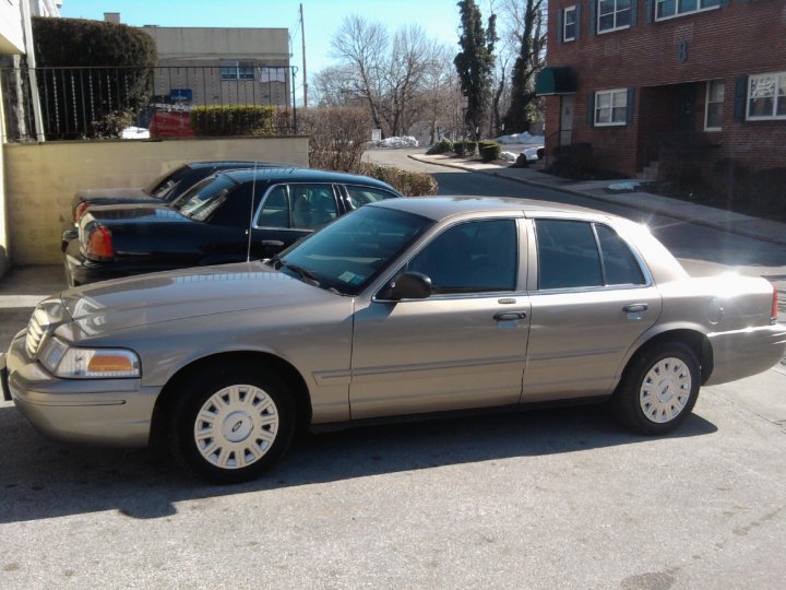 Tan-gray Ford Crown Victoria sedan parked in a paved lot