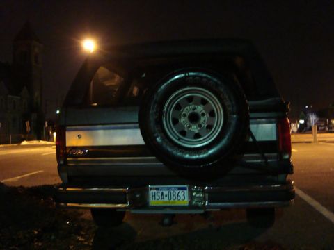 1991 Ford Bronco - Rear view of a 1991 Ford Bronco at night, showing the spare tire and license plate.