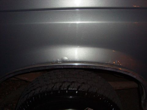 1991 Ford Bronco - Damage to the rear wheel well and fender of a gray vehicle.