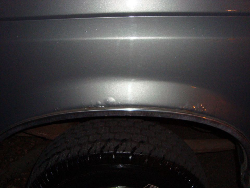 Close-up of a dent and rust on the rear wheel well of a gray vehicle