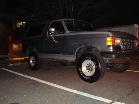 1991 Ford Bronco - This Ford Bronco is parked in a lot at night, showing its side profile and front end.