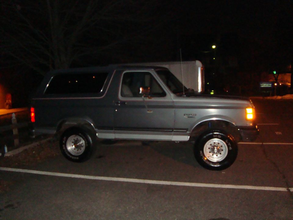 Gray Ford Bronco parked at night, side view. Chrome wheels and trim are visible