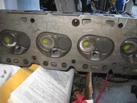 1981 Ford Bronco - Close-up view of an engine cylinder head, showing the valves and combustion chambers. Readable text is visible on documents in the foregrou…