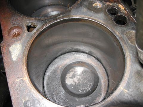 1981 Ford Bronco - Extreme close-up down a single cylinder bore with the head removed, showing a carbon-caked dished piston at mid-stroke and a visible ridge…