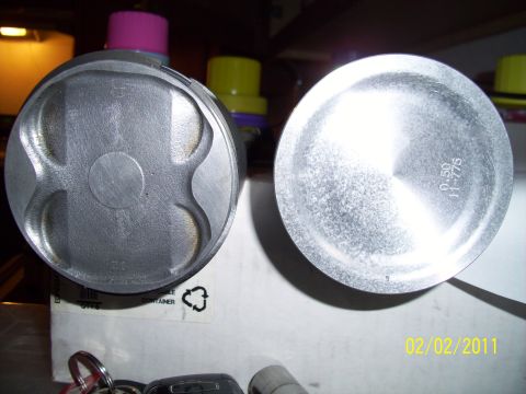 1995 Ford Probe - Close-up of two engine pistons, one showing valve reliefs, with keys and a box in the foreground.