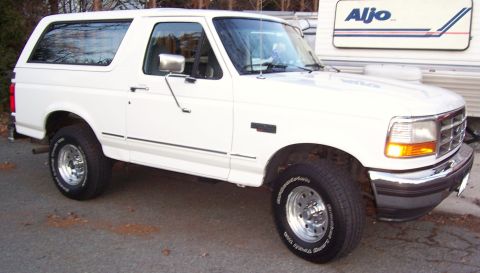 1996 Ford Bronco - A white 1996 Ford Bronco is parked on a paved surface, with a trailer visible in the background.