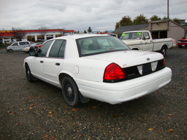White 2003 Ford Crown Victoria sedan, rear 3/4 view, parked on gravel lot