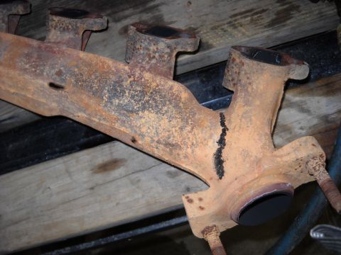 1993 Ford C-150 (Centurion Conversions) - A heavily rusted exhaust manifold is shown, resting on wooden planks.