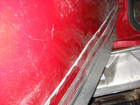 1993 Ford C-150 (Centurion Conversions) - Close-up of a damaged red door panel, showing scratches and a dented lower section.