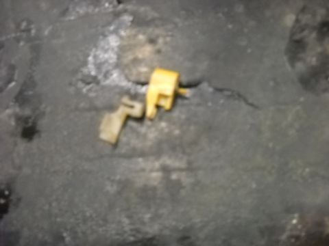 1993 Ford C-150 (Centurion Conversions) - Two plastic door lock actuator clips, one yellow and one tan, are shown on a dark, textured surface.