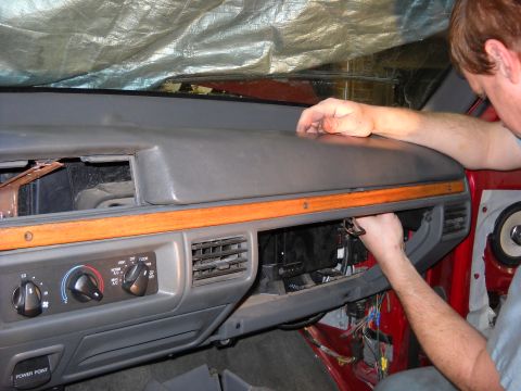 1993 Ford C-150 (Centurion Conversions) - Close-up of a vehicle's interior dashboard and climate controls, with a person accessing wiring beneath the dash.