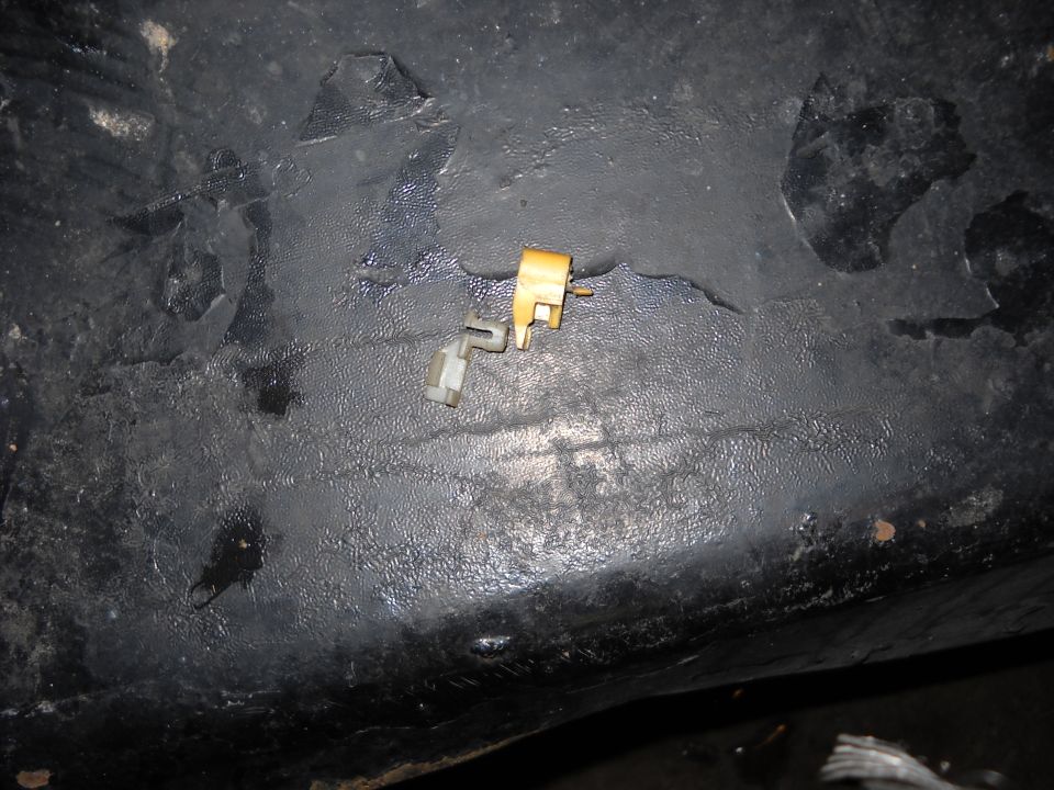 Close-up of a small plastic and metal door lock actuator component on a dark, textured surface